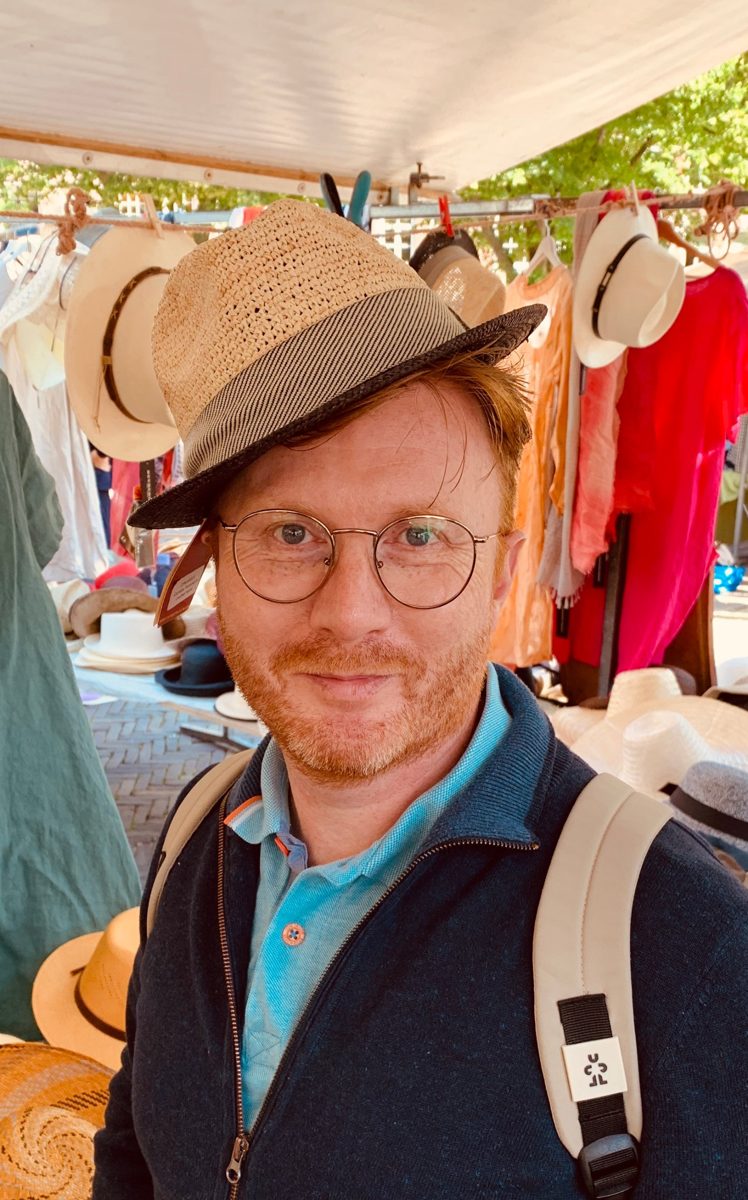 Jürgen probiert auf einem Markt einen Strohhut an