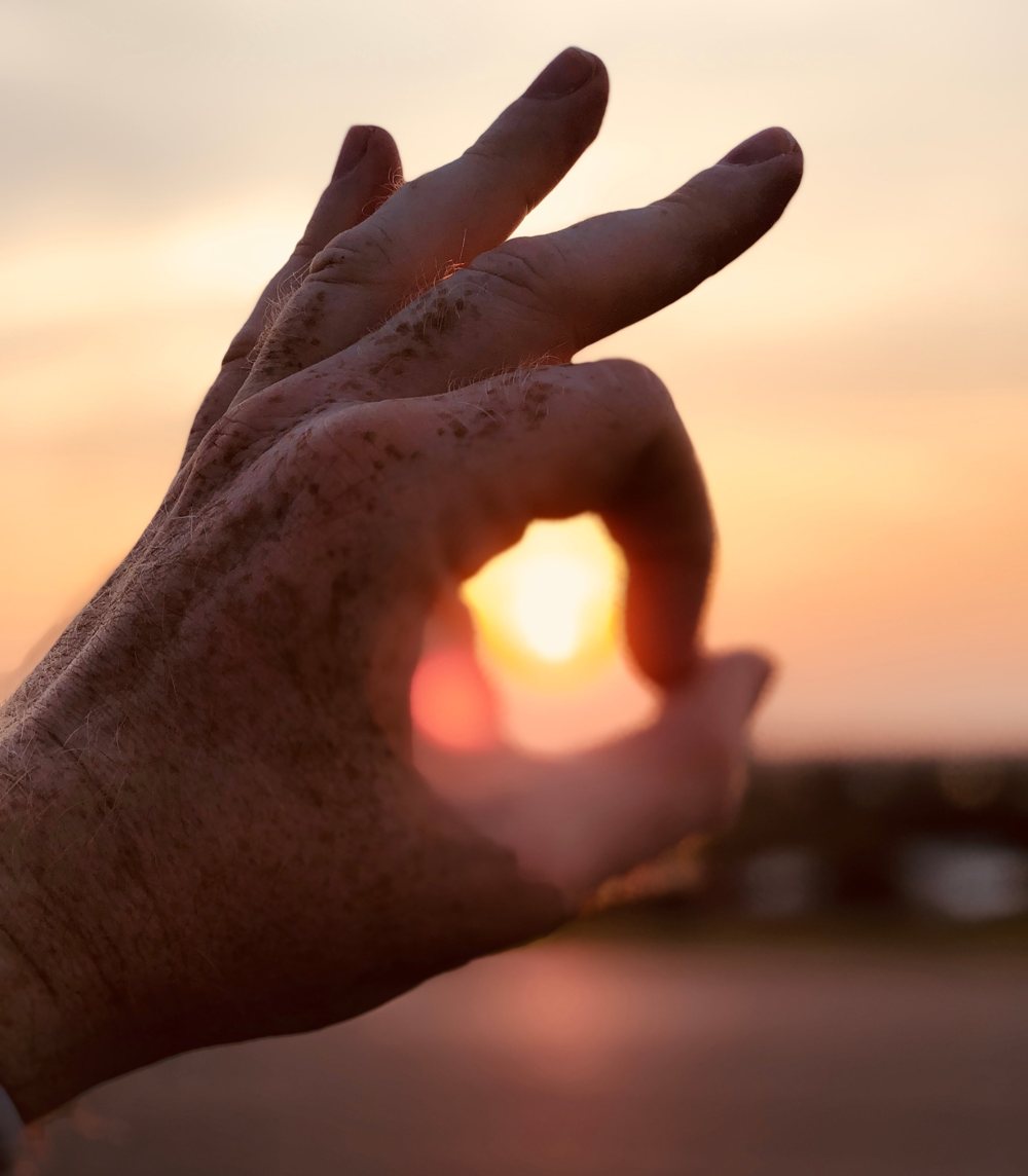 Eine Hand formt einen Kreis, in dem die Abendsonne leuchtet